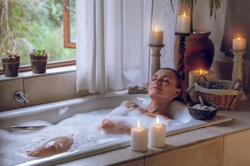 Woman relaxing in bubble bath surrounded by candles in serene bathroom