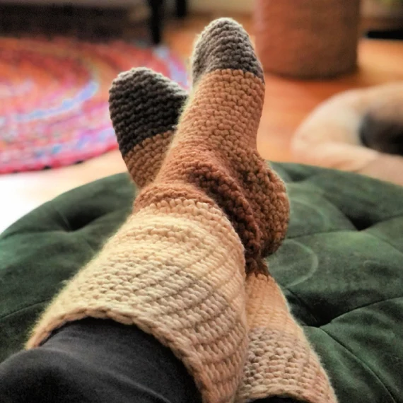 Cozy crochet slipper socks in neutral stripes on green ottoman
