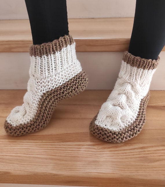 Hand-knit white and brown cable-knit house slippers on wooden stairs — cozy chunky wool booties with folded cuff