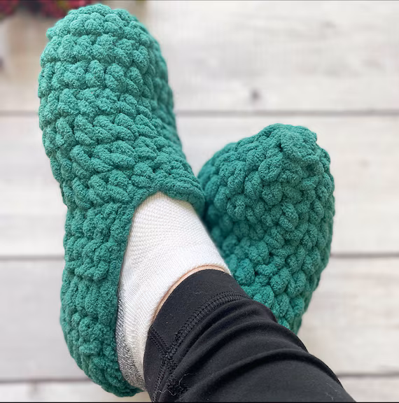 Fuzzy emerald green chunky knit slippers on white wooden floor — bright handmade house footwear with textured stitch.