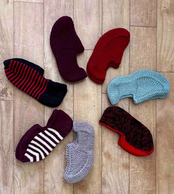 alt="Collection of handmade knitted wool slippers in different colors and patterns on wooden floor"