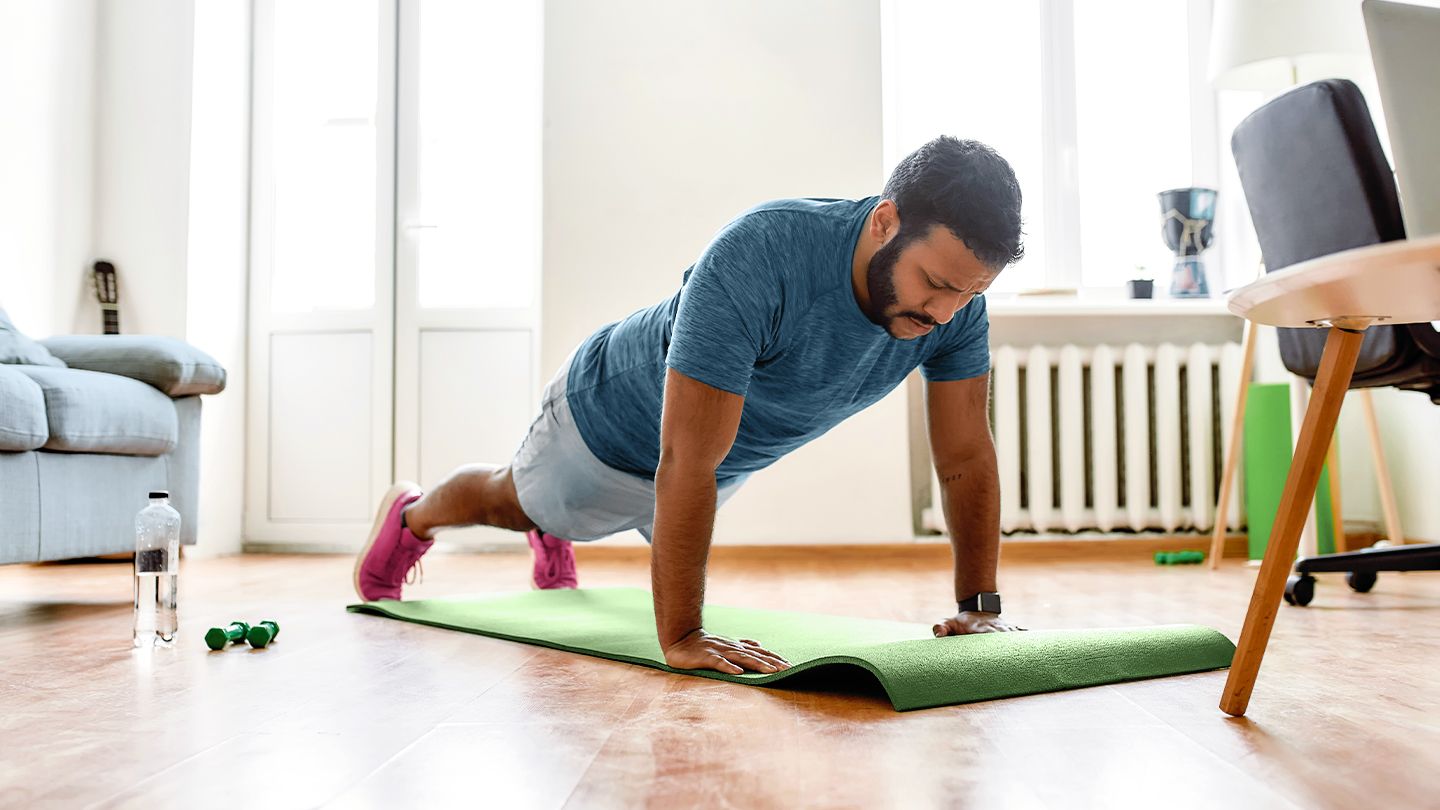 Man doing push-up on green yoga mat in living room at home