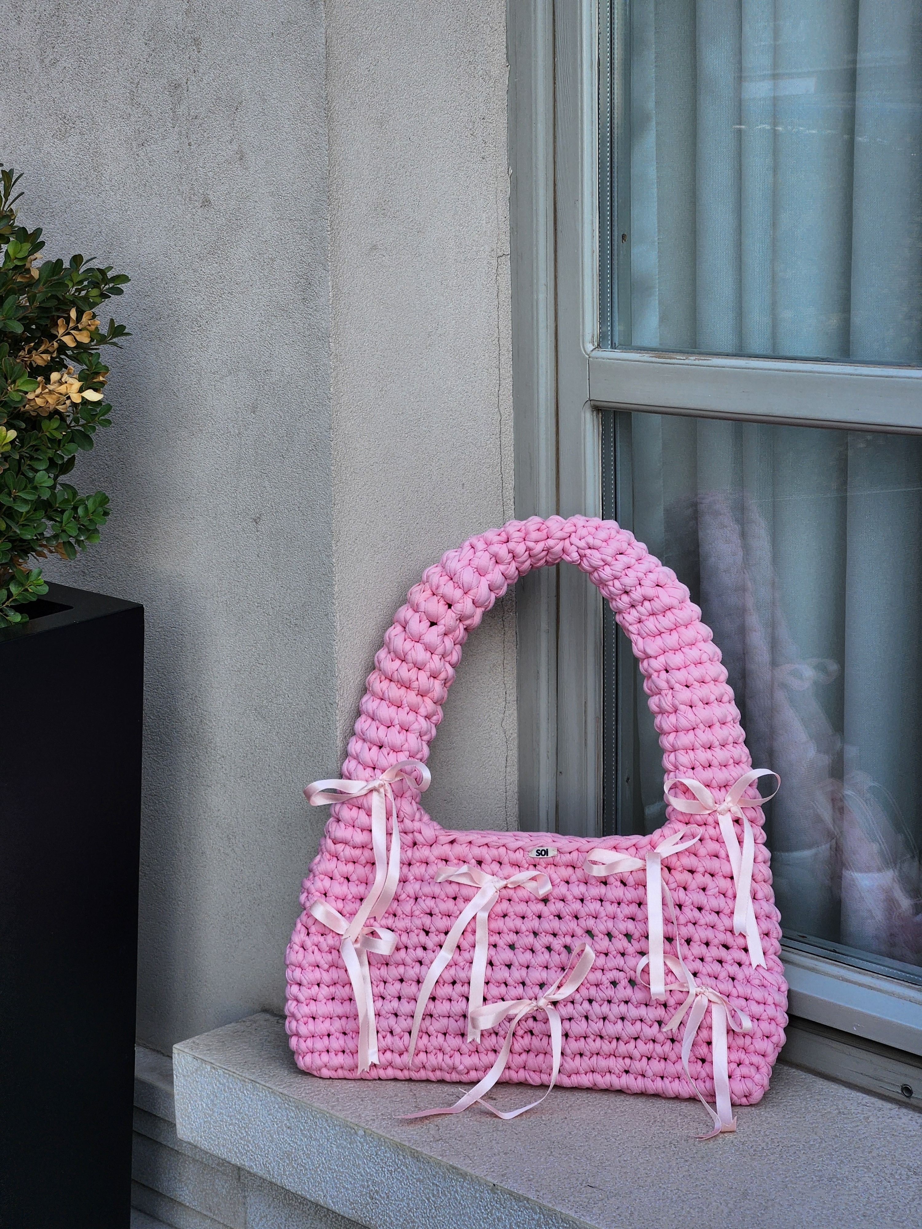 Handmade color-blocked crochet tote bag in pink, peach and lavender with tassel, leather tag and QR code pattern label on marble surface