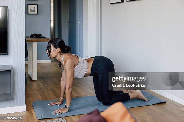 Woman practicing cat-cow yoga pose on mat in bright modern home interior
