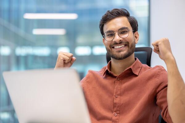 Happy young professional celebrating success at desk in modern office  setting. Showing excitement and achievement while working on laptop.  Positive work environment and career growth concept. 56499927 Stock Photo  at Vecteezy