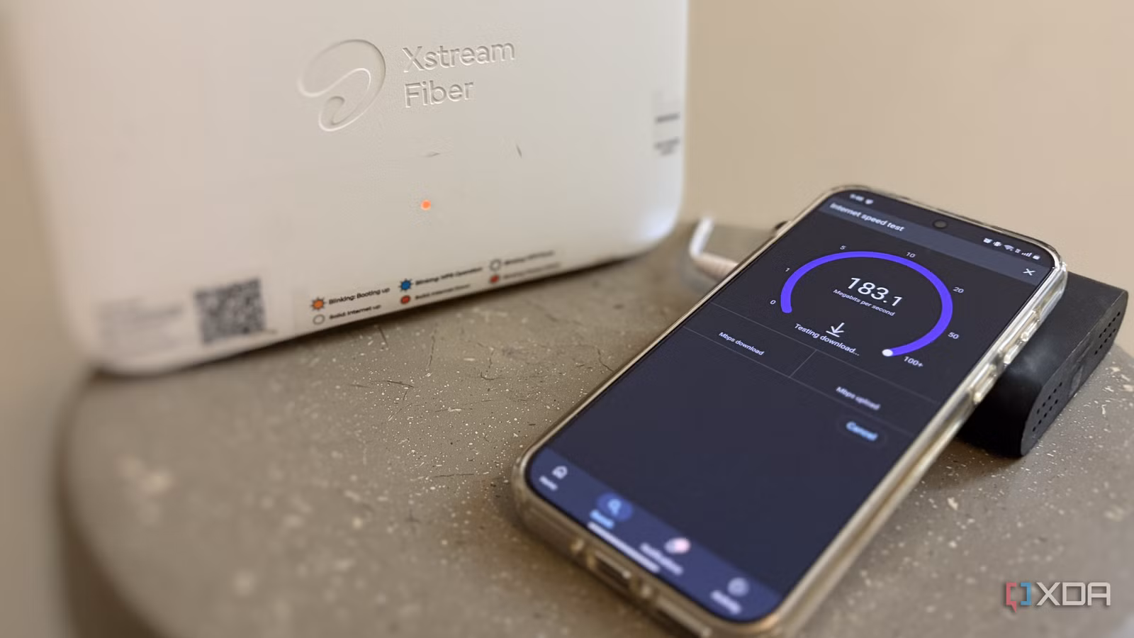 Smartphone running a speed test next to a fiber internet router on a desk