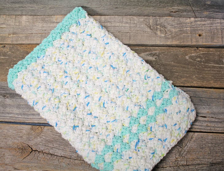 Terracotta crochet hand towel hanging on brass hook by white farmhouse sink — handmade cotton towel in sunny kitchen with herbs